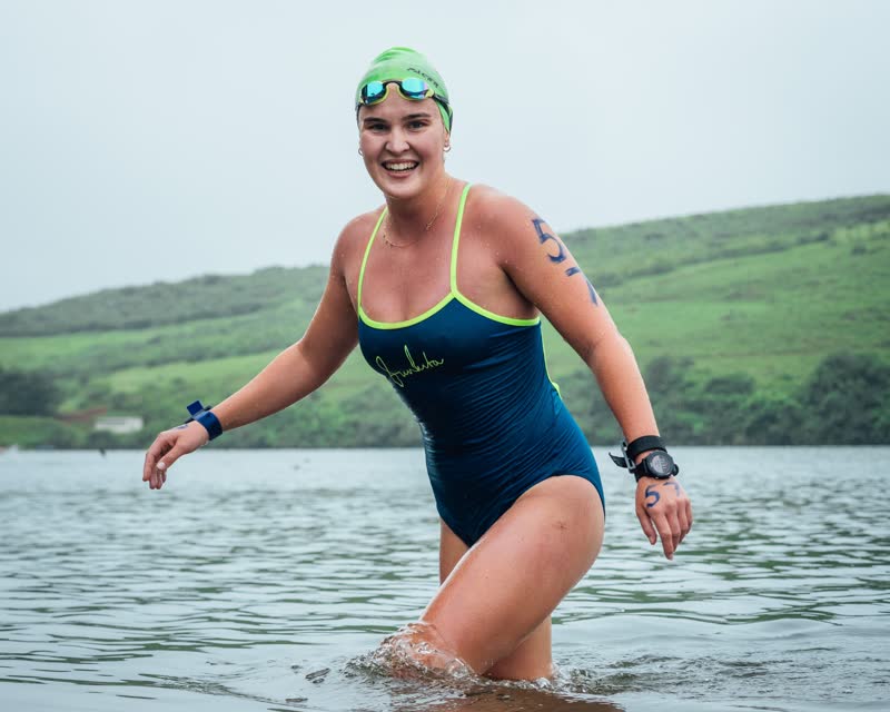 Swimmer in a green cap smiling while wading out of the water at the Bainsfield Swim