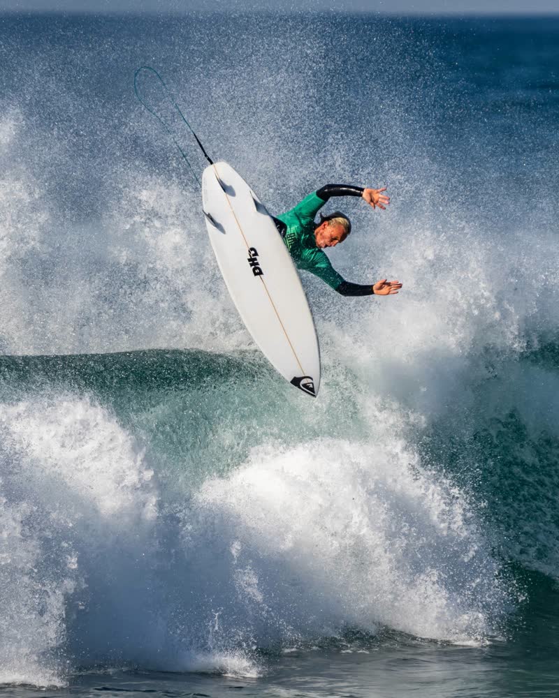 Surfer in a green vest launching an aerial above a breaking wave at the Ballito Pro