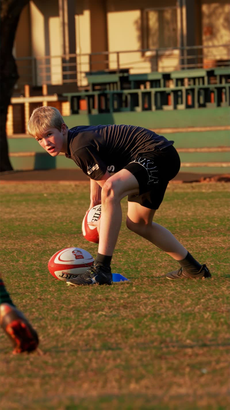 Jordy Rom crouching to pick up a rugby ball at training in late-afternoon light